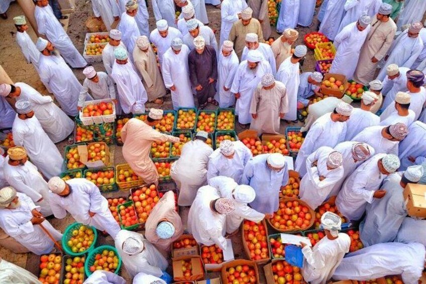 A market scene with people in white robes and head coverings, surrounded by various fruits and vegetables. 2