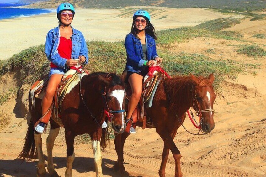 Due persone a cavallo su una spiaggia sabbiosa, con vista sull'oceano e delle colline sullo sfondo. 5