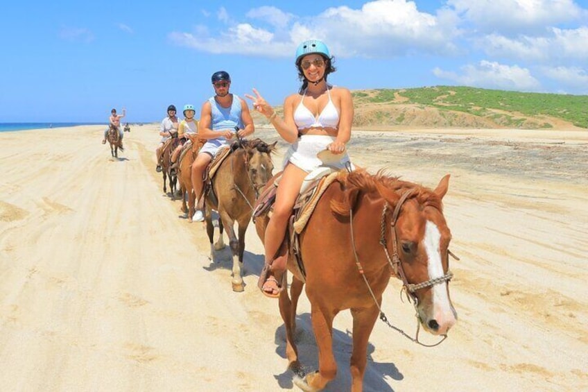 Un gruppo di persone cavalca lungo una spiaggia sabbiosa sotto un cielo sereno. 1