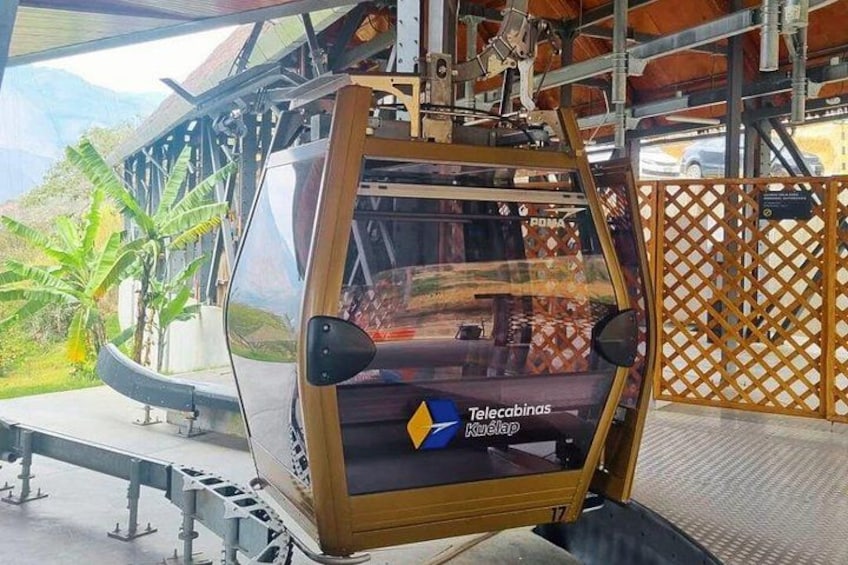 A cable car with 'Telecabinas' and 'Kuelap' logos, suspended by cables, with a mountainous landscape in the background. 2