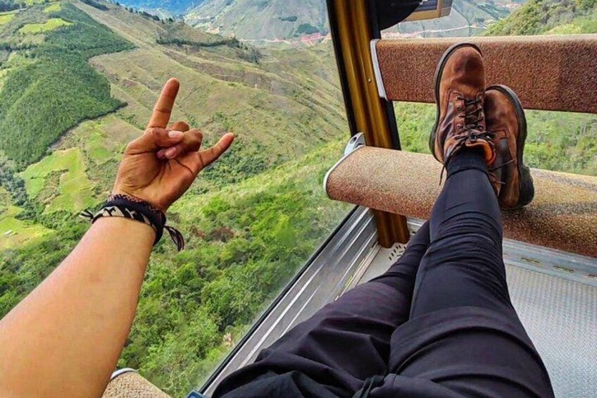 A person's legs and feet on a cable car, with a hand making a peace sign. 5