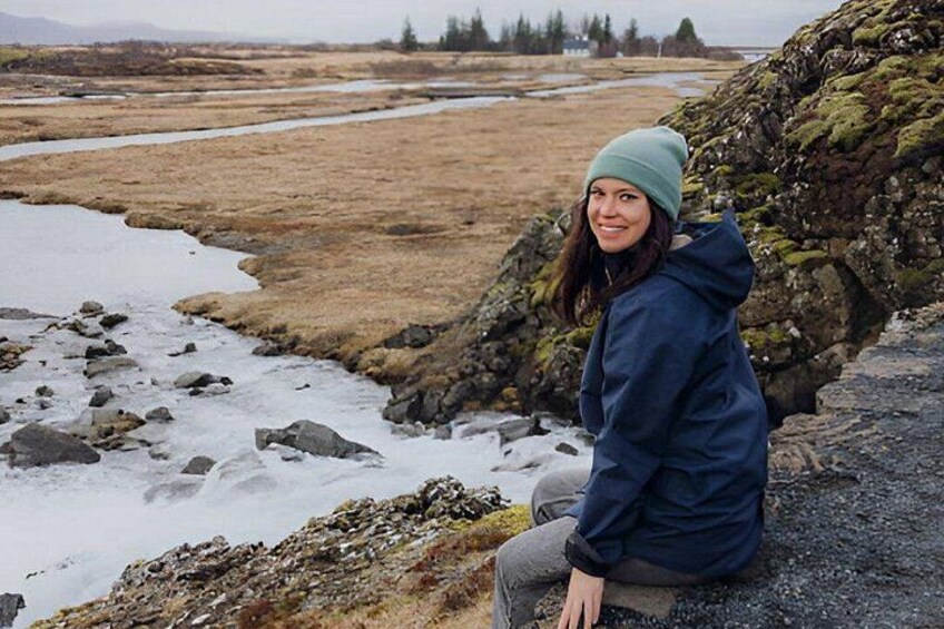 A person sitting on a rocky outcrop near a river with a grassy landscape in the background. 4