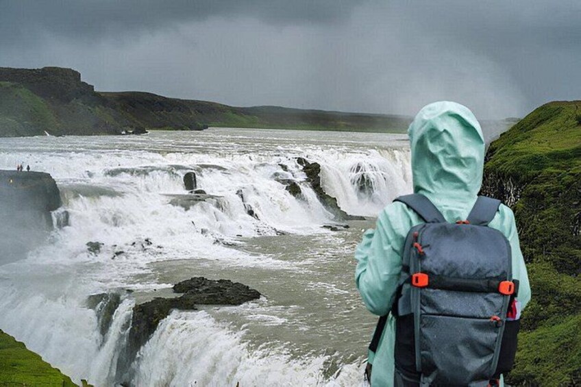 A waterfall with a person in a green jacket and a backpack. 1