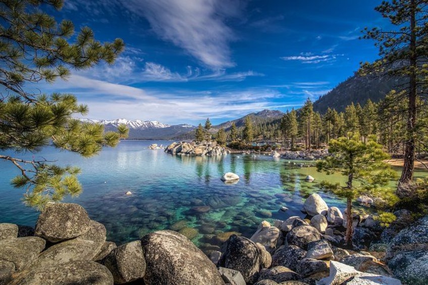 Un lago transparente rodeado de rocas y pinos, con montañas al fondo. 2
