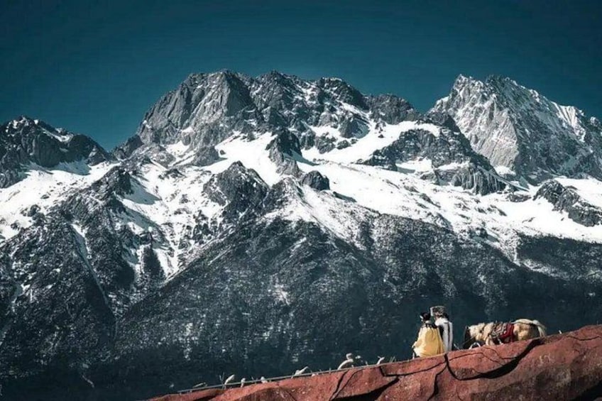 A mountain range with snow-covered peaks and a group of people on a red surface. 1