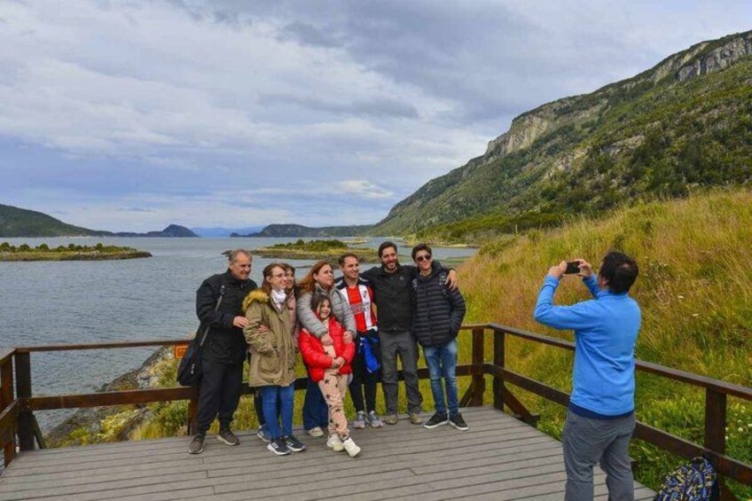 Een groep mensen op een houten terras met uitzicht op een meer, met bergen op de achtergrond. 5