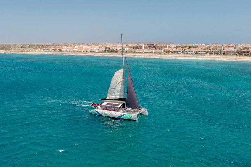 A sailboat on turquoise water with a beach and buildings in the background. 3