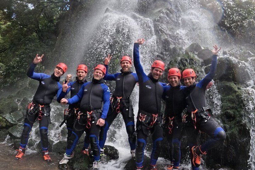 Een groep mensen in blauwe zwempakken en rode helmen poseren voor een waterval. 5