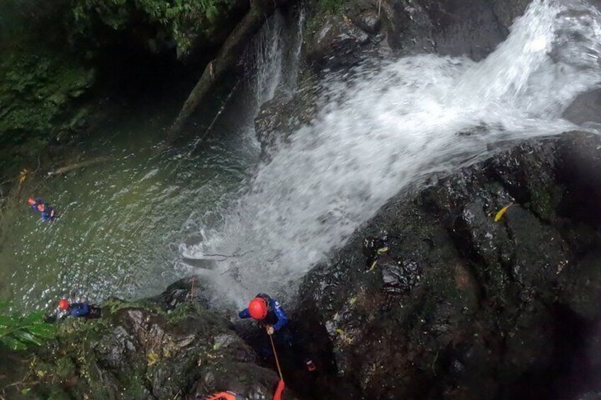 Een waterval met water dat over rotsen stroomt, een persoon in blauwe en rode kleding in de buurt van het water, en nog een persoon op de achtergrond. 3