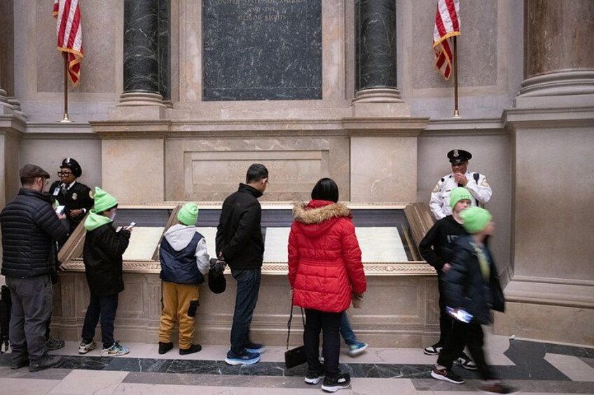 A group of people standing in line outside a building with a marble facade and columns. 3