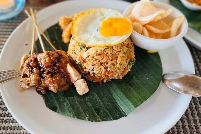 A plate of fried rice with a fried egg on top, accompanied by a side of meat and a small bowl of crackers. 1