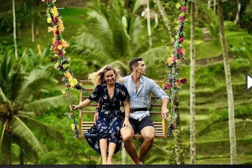 Two people on a swing decorated with flowers, surrounded by lush greenery. 2