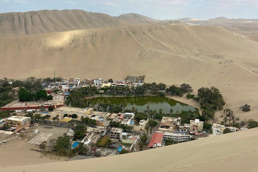 Paesaggio desertico con un piccolo insediamento, un'area d'acqua e dune sabbiose. 4