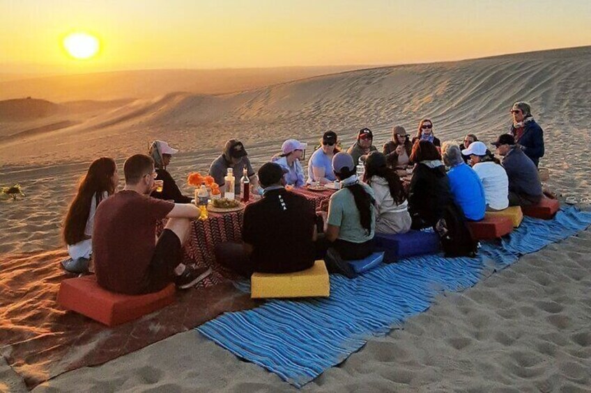 Un gruppo di persone sedute su coperte in un deserto al tramonto. 5