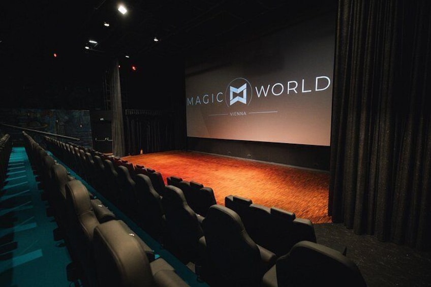 An indoor cinema with rows of seats and a large screen displaying 'MAGIC WORLD VIENNA'. 4