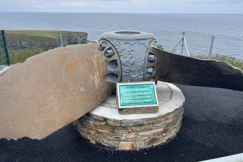 A large stone monument with a plaque, set against a coastal backdrop. 4