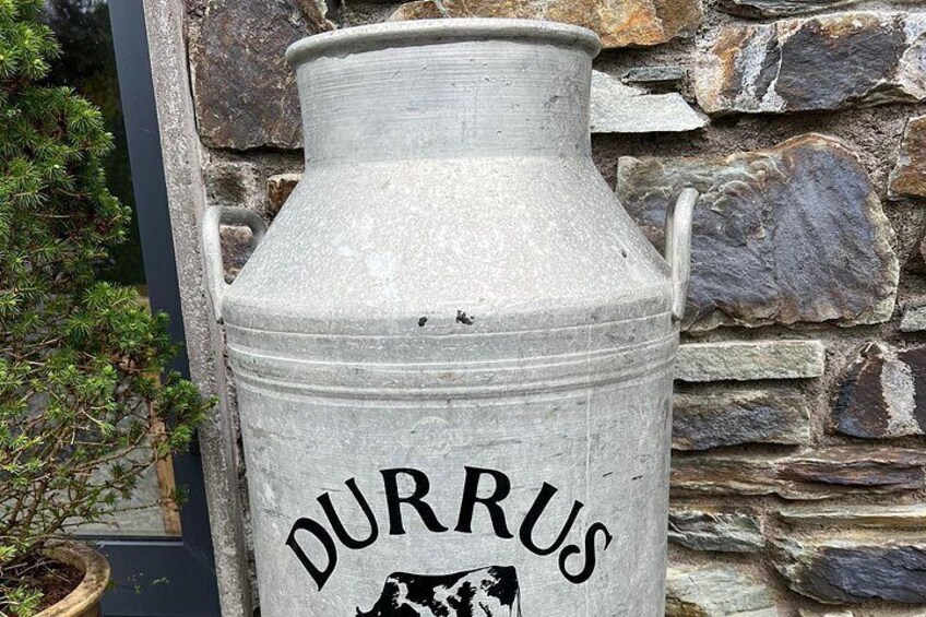 A large metal container labeled 'DURRUS' with a cow illustration, set against a stone wall background. 5