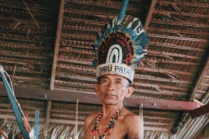 A person wearing a feathered headdress with the inscription "BRU PATAU" and a necklace. 1