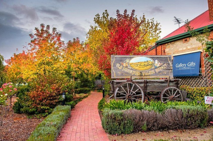 A pathway leading to a sign for Old Hampton Village Market, surrounded by autumn-colored trees and a brick building. 2