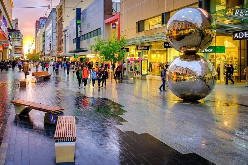 A busy urban square with people walking, benches, and a large reflective sculpture. 3