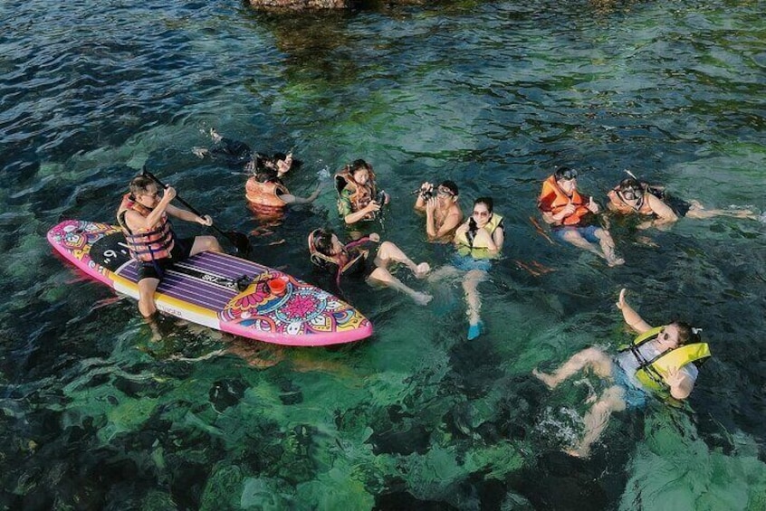 A group of people snorkeling in clear water, some on a colorful surfboard. 2