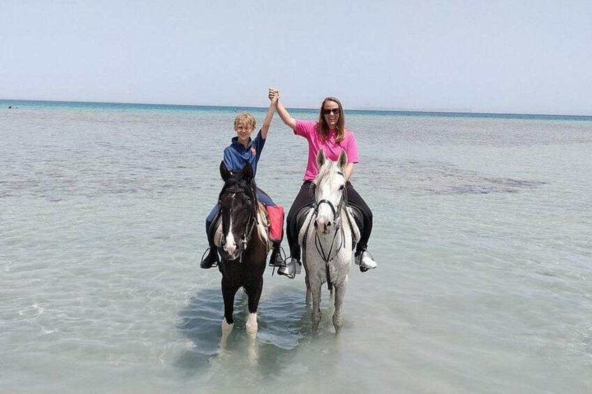 Two people riding horses in shallow water. 1
