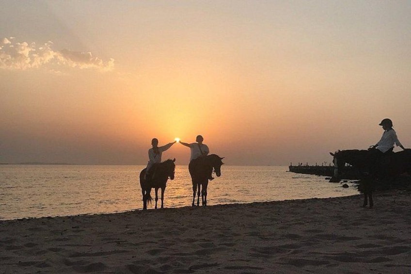 A sunset over a beach with people on horseback. 5