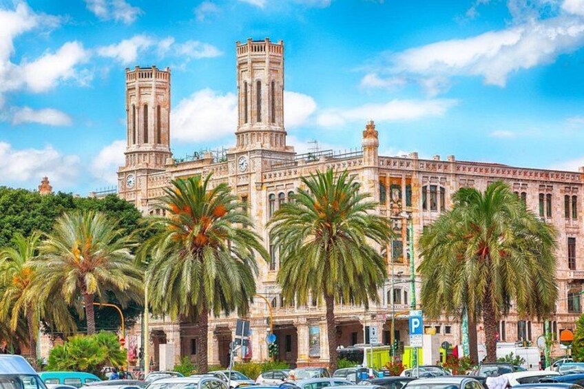 Un edificio histórico con dos torres, palmeras y coches aparcados. 3