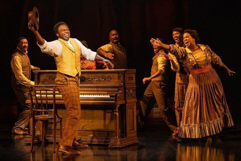 A theater stage with actors in period costumes, a piano, and a wooden bench. 5