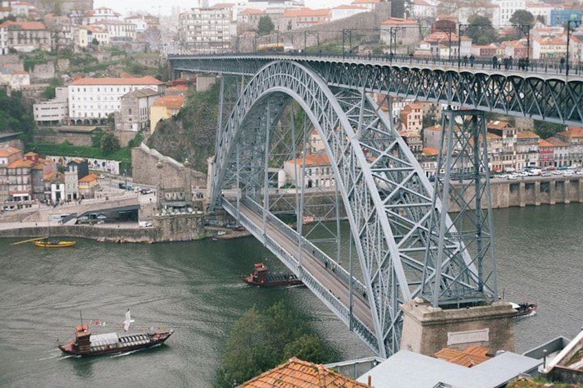 A large steel bridge spanning a river, with buildings and a boat in the foreground. 3