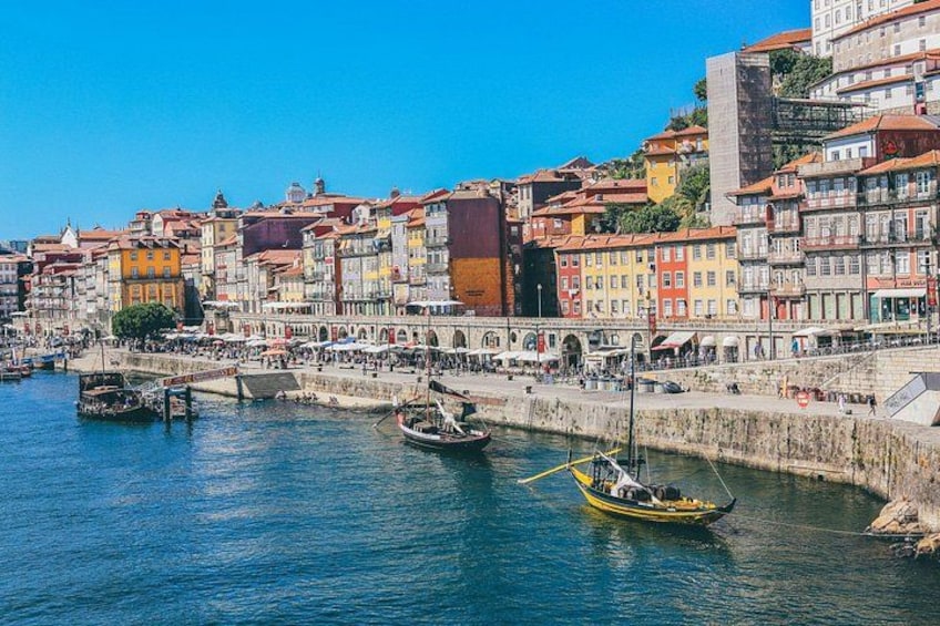 A waterfront cityscape with colorful buildings, boats, and a stone wall. 1