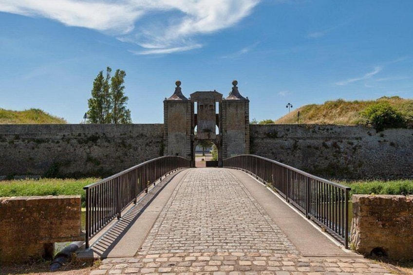A cobblestone bridge leading to a historic stone gate with two towers. 2