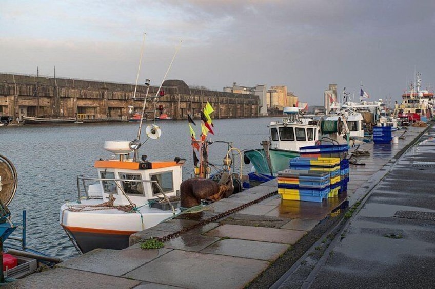 A harbor with boats docked along the piers, a large industrial structure in the background, and a cloudy sky. 3