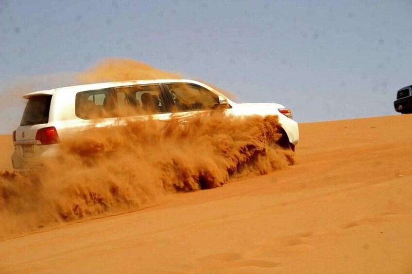 A white SUV driving through a desert with sand being kicked up by its tires. 3