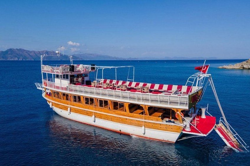 A large boat with a red and white striped deck, a flag, and a mountainous landscape in the background. 1