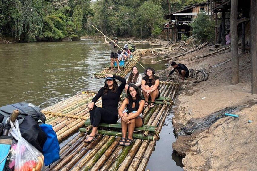 People on a bamboo raft on a river, surrounded by trees and a wooden structure. 3
