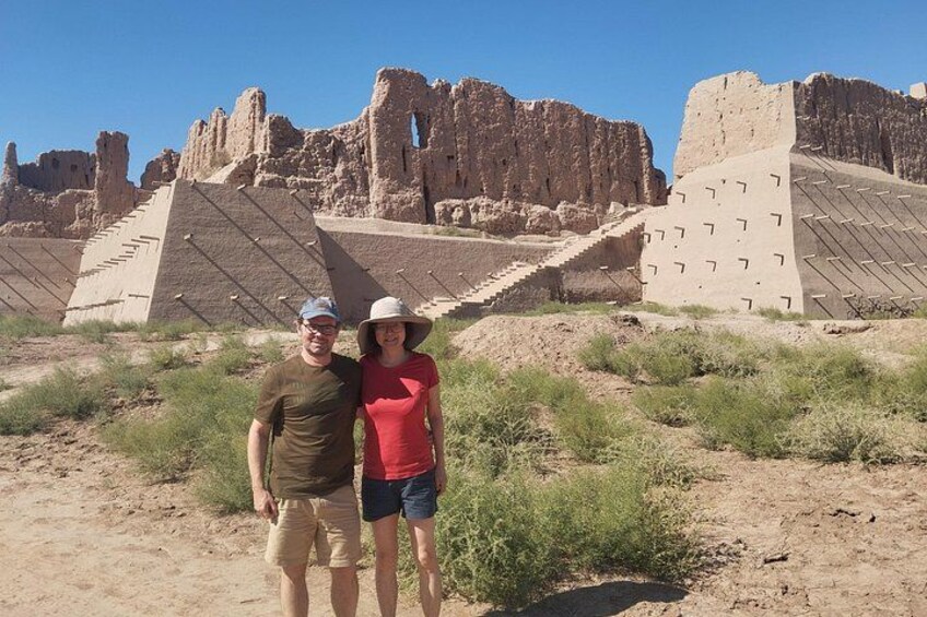 Dos personas de pie frente a ruinas antiguas con pirámides escalonadas y una gran estructura de piedra. 5