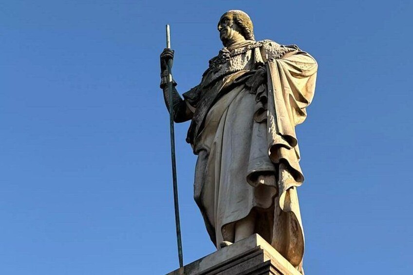 Eine Statue einer Person, die eine Stange hält und auf einem Sockel vor blauem Himmel steht. 5