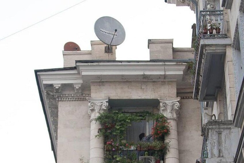 Un immeuble doté d’une antenne parabolique, d’un balcon orné de fleurs et de détails architecturaux classiques. 2