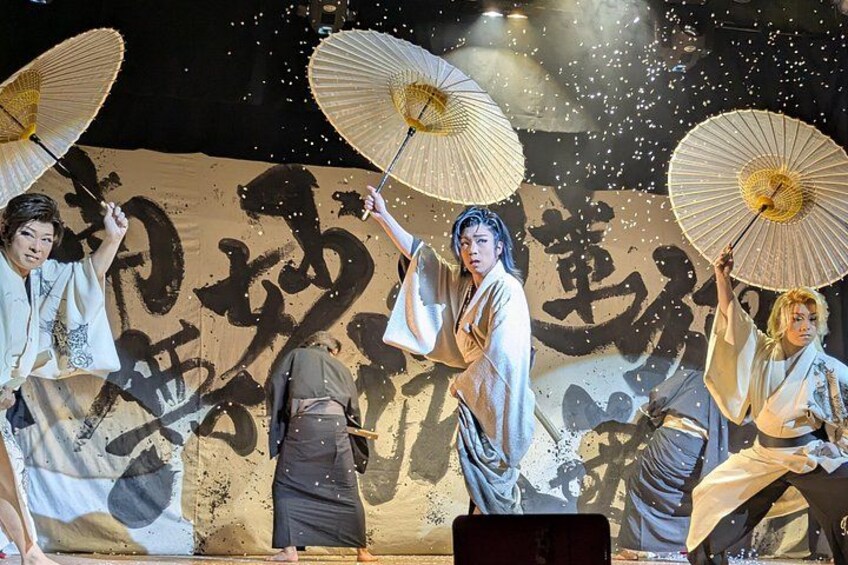 Performers in traditional attire with fans, a backdrop with calligraphy, and a stage setting. 5