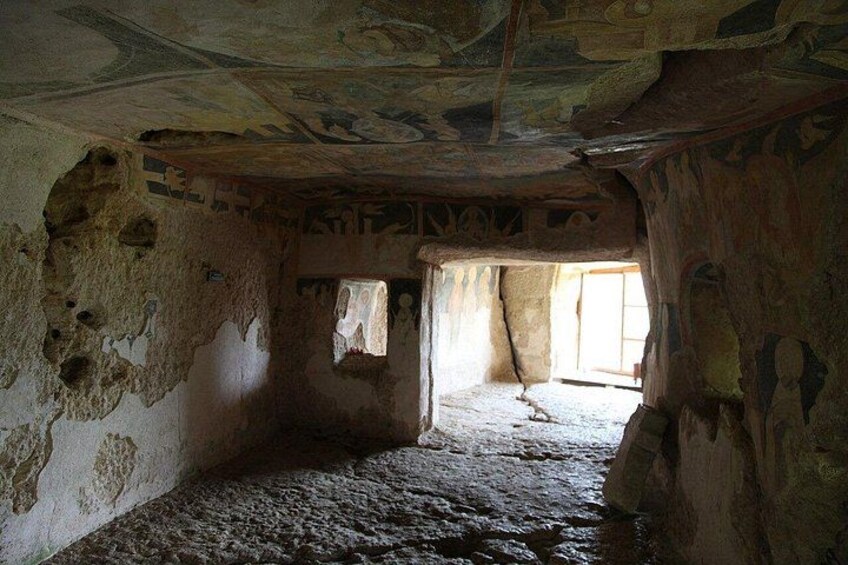 An ancient, dilapidated room with a stone floor, rough walls, and a ceiling with faded frescoes. 4