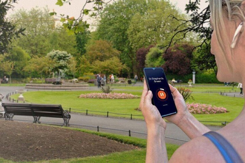 A person holding a smartphone with a green park in the background. 5