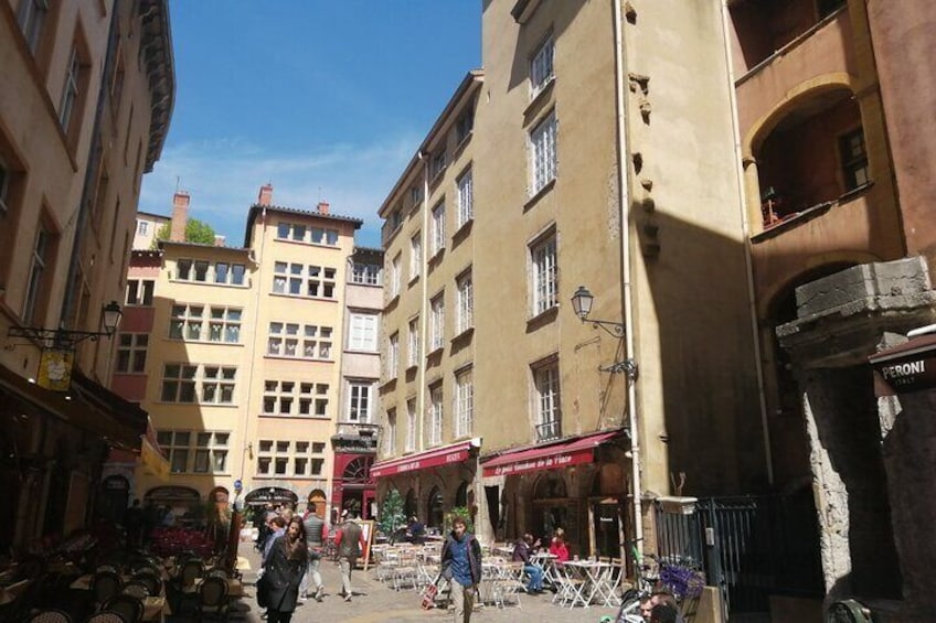 Una calle estrecha con edificios, un café y gente caminando. 3