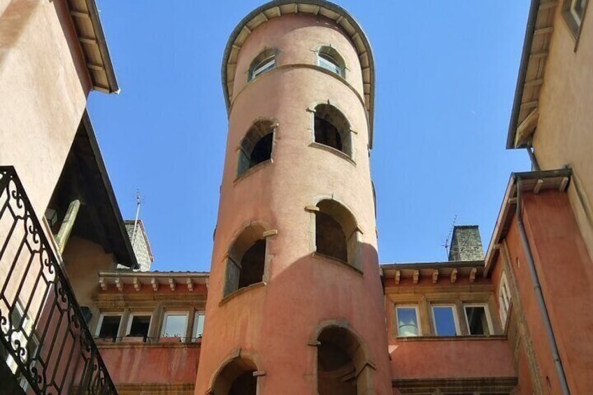 Una torre alta y cilíndrica con ventanas de arco y una parte superior redondeada, rodeada de edificios con un estilo arquitectónico similar. 5
