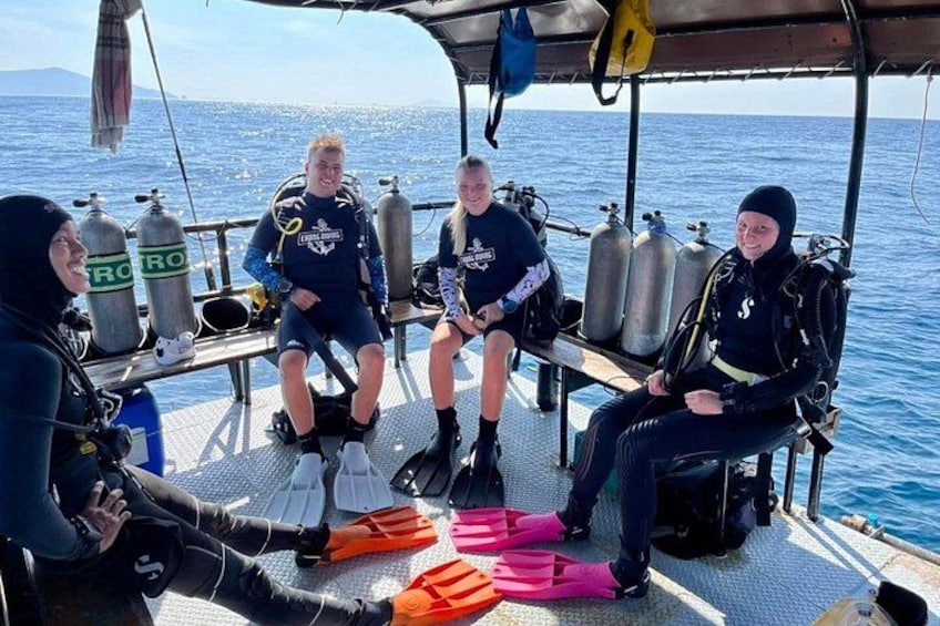 Four people in scuba diving gear on a boat, with oxygen tanks and fins. 4