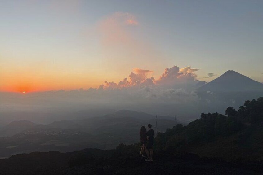A sunset over a mountain range with a person standing on a hill. 4