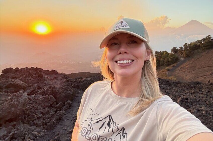 A person wearing a cap and a t-shirt with a mountain design, standing on a rocky terrain with a sunset in the background. 5