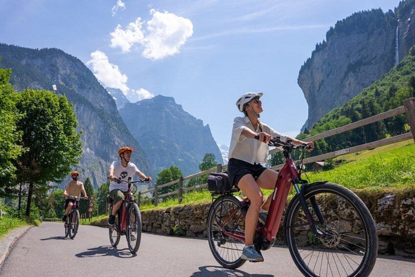 Three cyclists on a paved path with a mountainous landscape in the background. 4