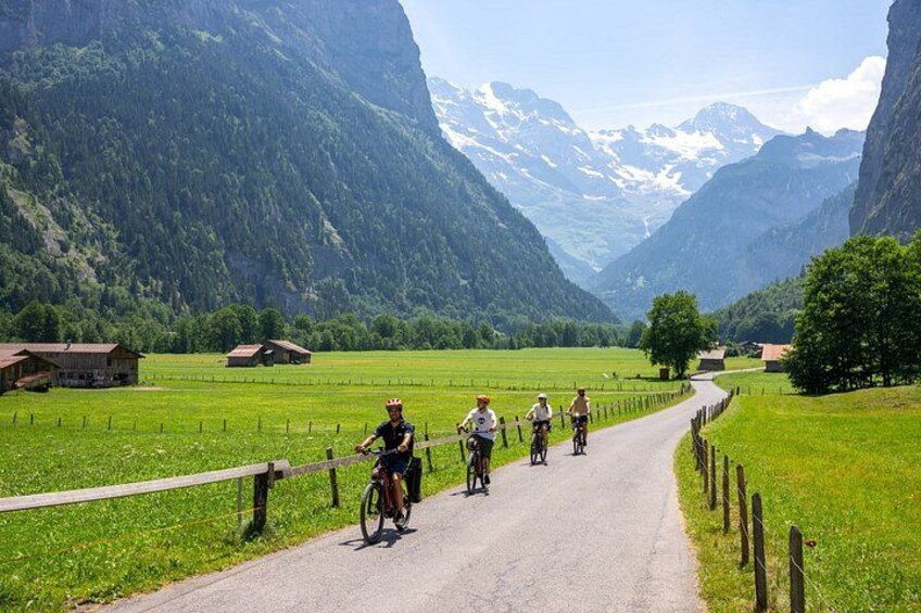 Cyclists on a paved road with green fields and mountains in the background. 5