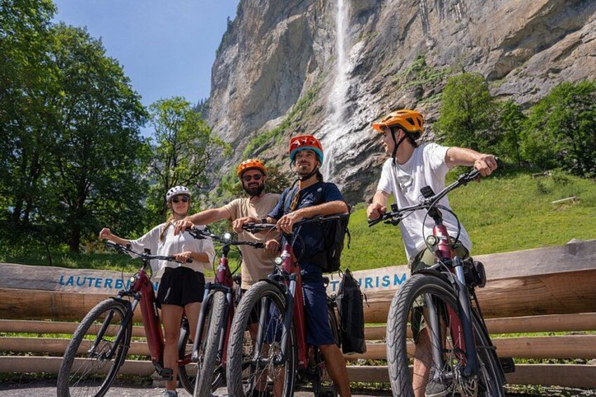 Four people on bicycles with a waterfall and trees in the background. 1